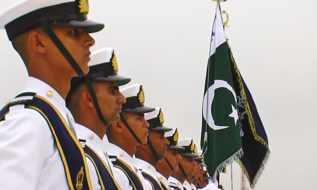 Pakistan Naval officers standing next to a flag
